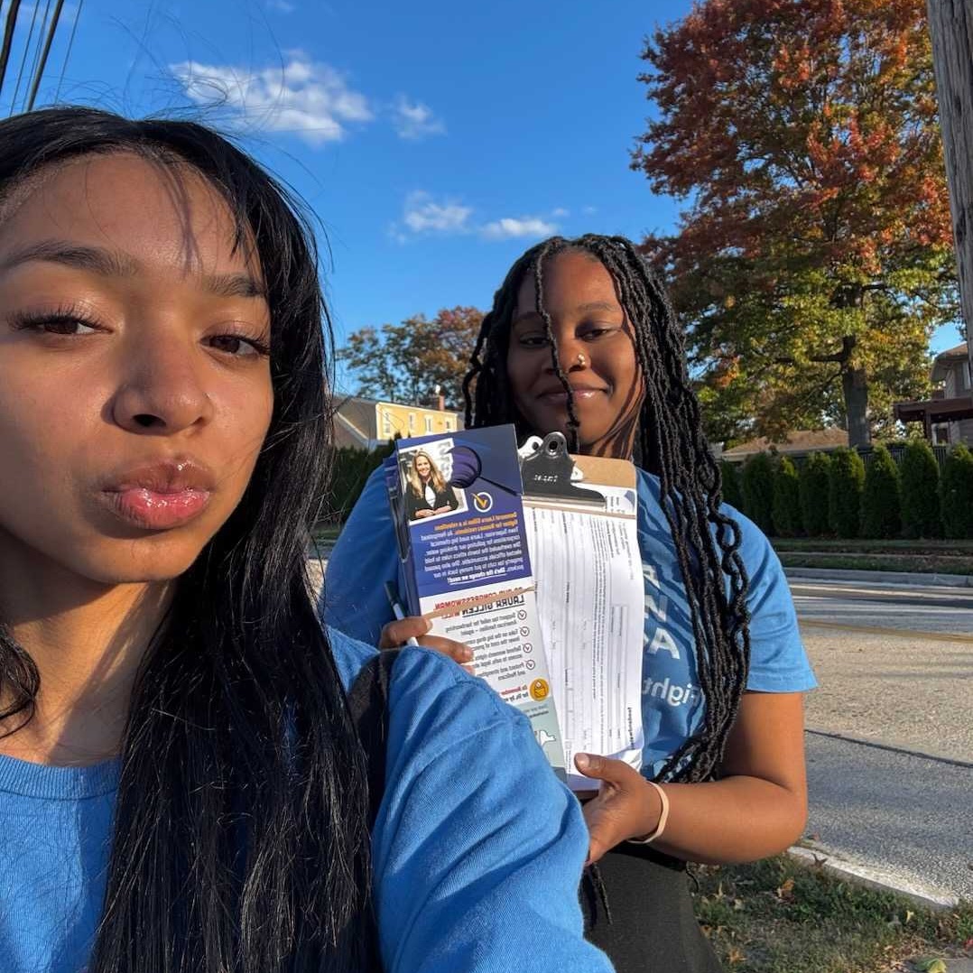 Two young women of color wear blue Food & Water Action shirts and pose with a clipboard.