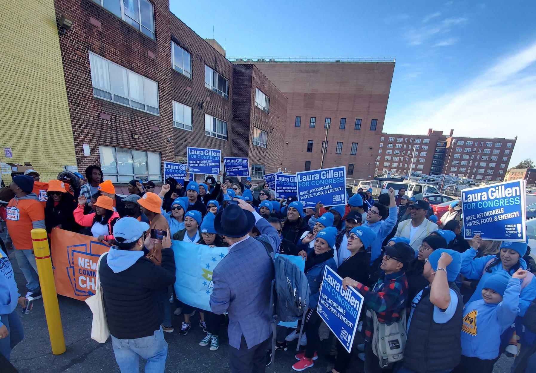 A crowd assembles in a parking lot holding signs that says "Laura Gillen for Congress."