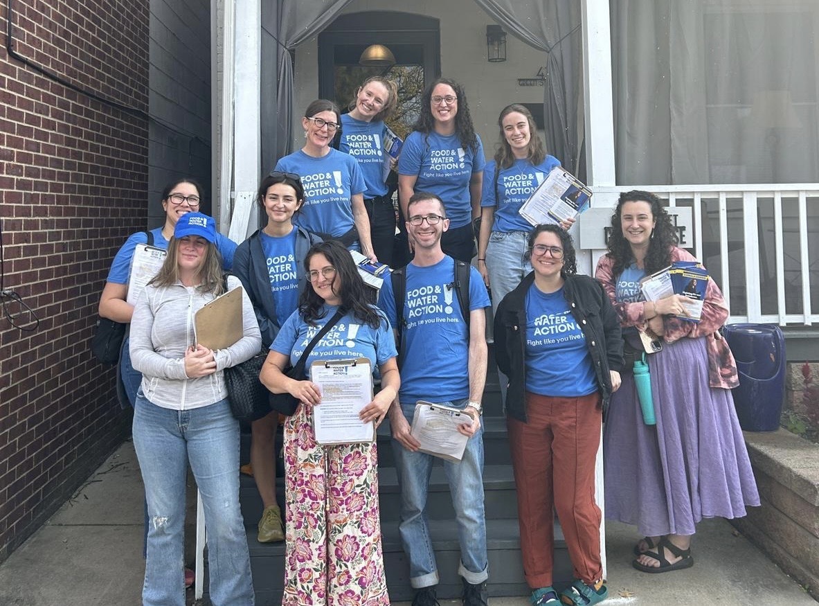 Eleven staff members pose on the steps of a house wearing "Food & Water Action!" shirts and carrying flyers and clipboards.